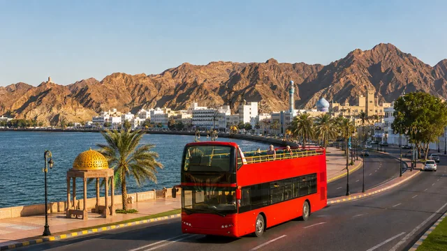 An open-top sightseeing bus beside the Muscat waterfront
