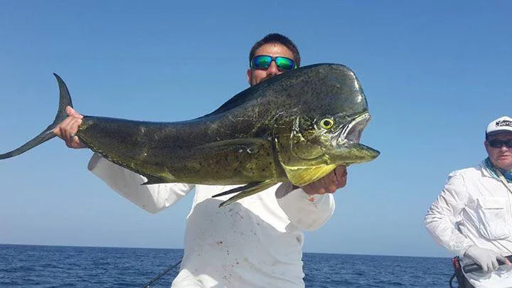 An angler holding a fish beside the sea