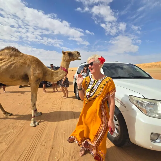 A traveller beside a camel and vehicle in the dunes